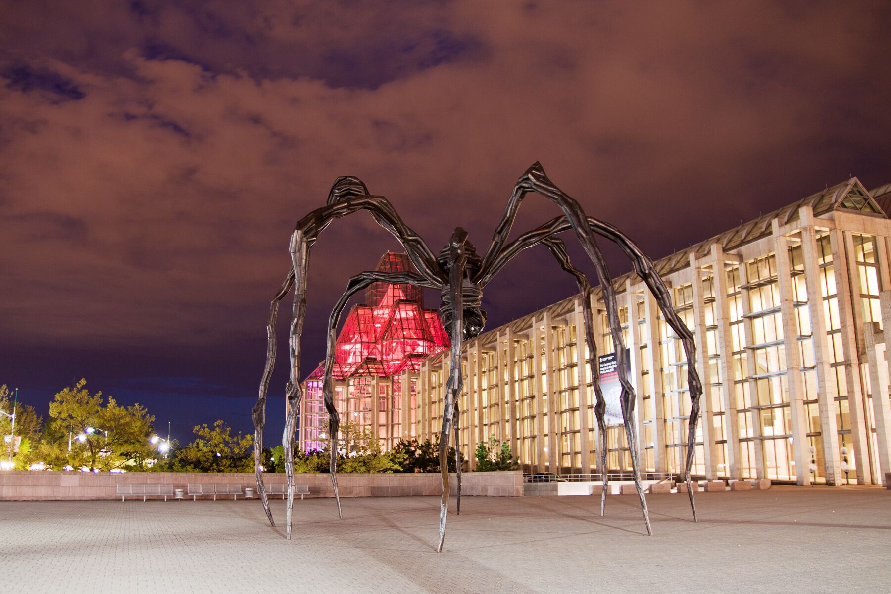 A large metal sculpture of a spider in front of a building with a glass facade.