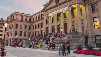 A historic building with classical architecture, a central staircase, and a crowd of people gathered outside.