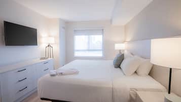 Une chambre d’hôtel moderne dotée d’un grand lit, de lampes de chevet, d’un téléviseur à écran plat et d’une fenêtre avec des stores.