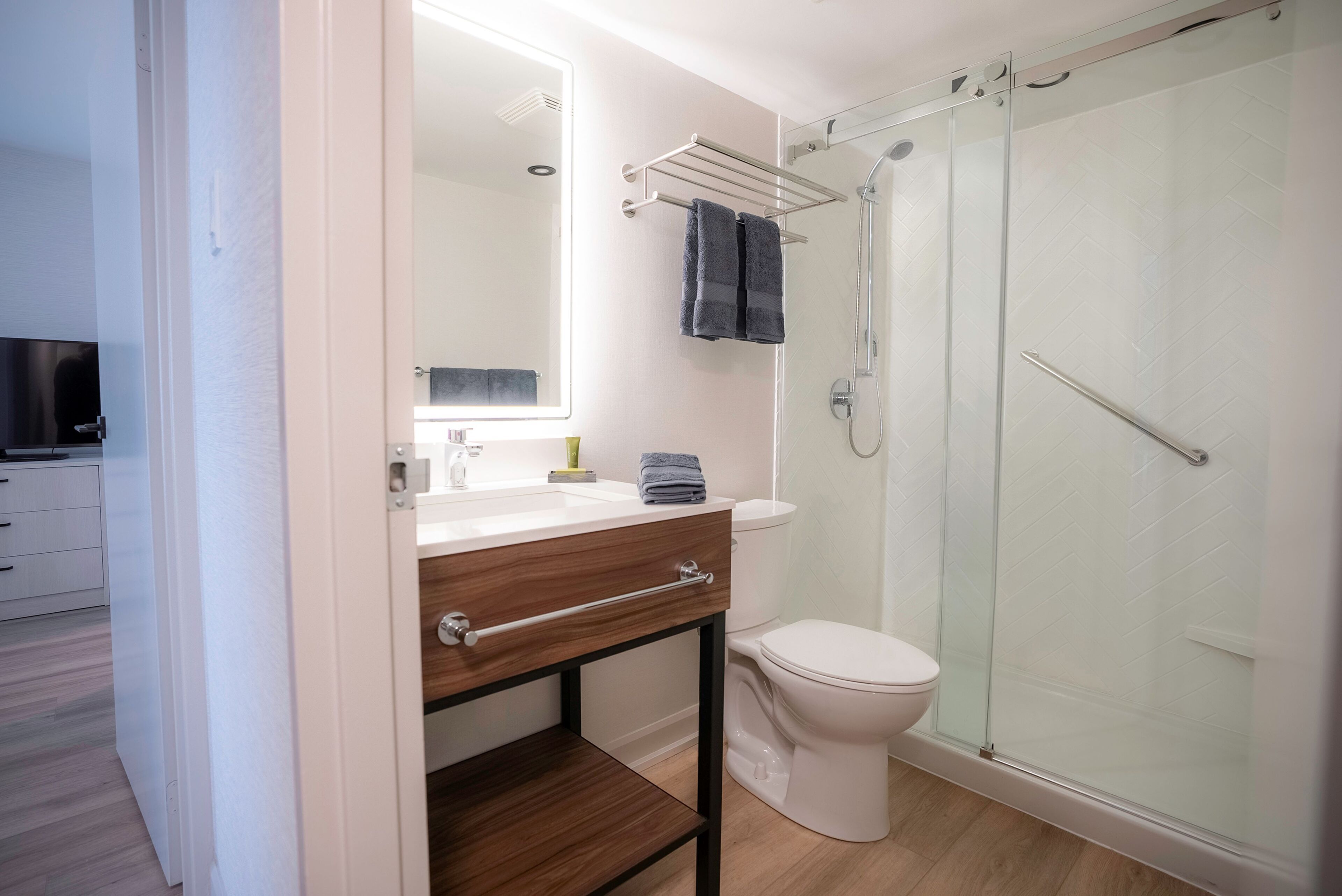 A modern bathroom with a glass shower enclosure, a white toilet, and a wooden vanity with a mirror.