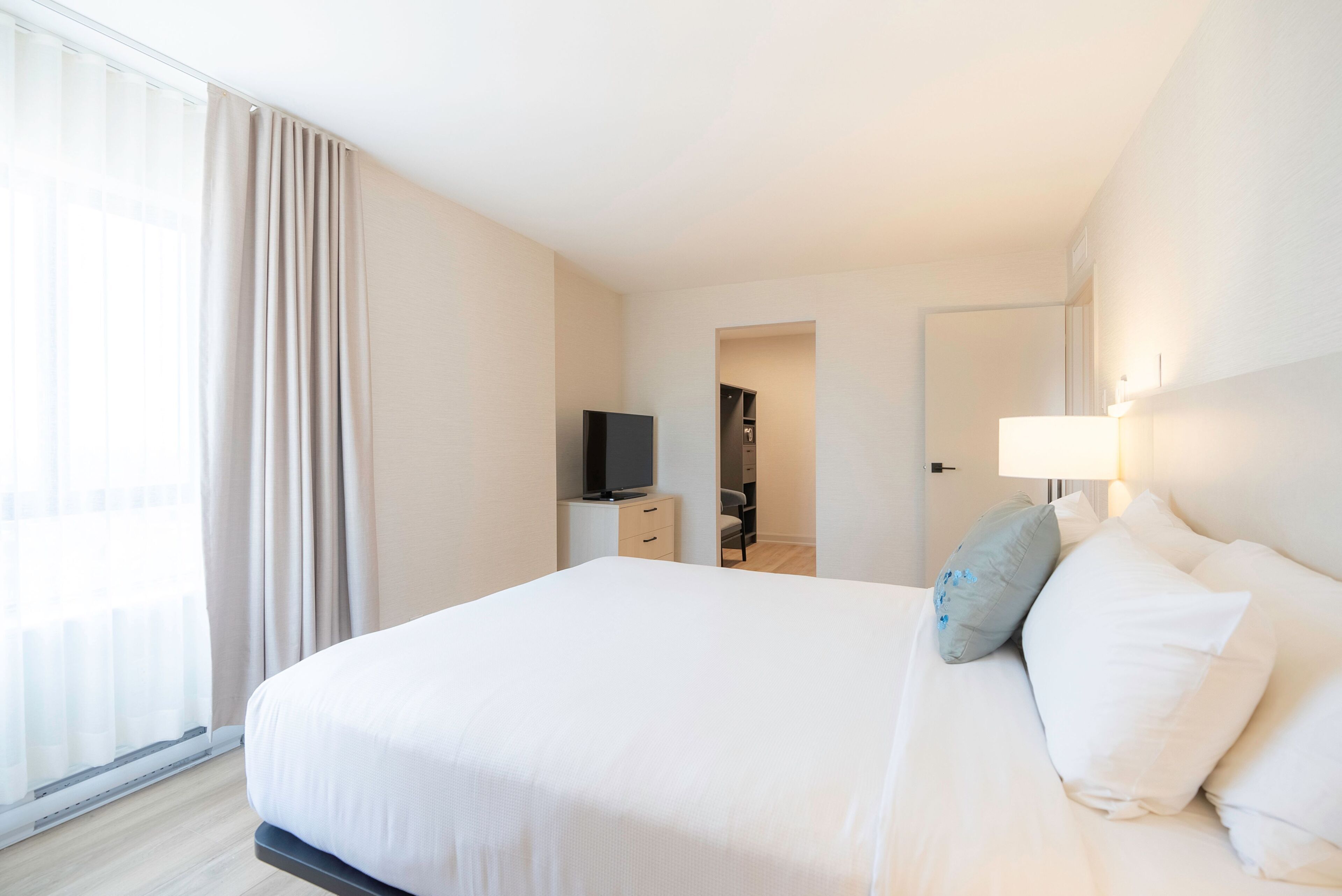 Quarto de hotel com uma cama grande, televisão, escrivaninha e abajur.