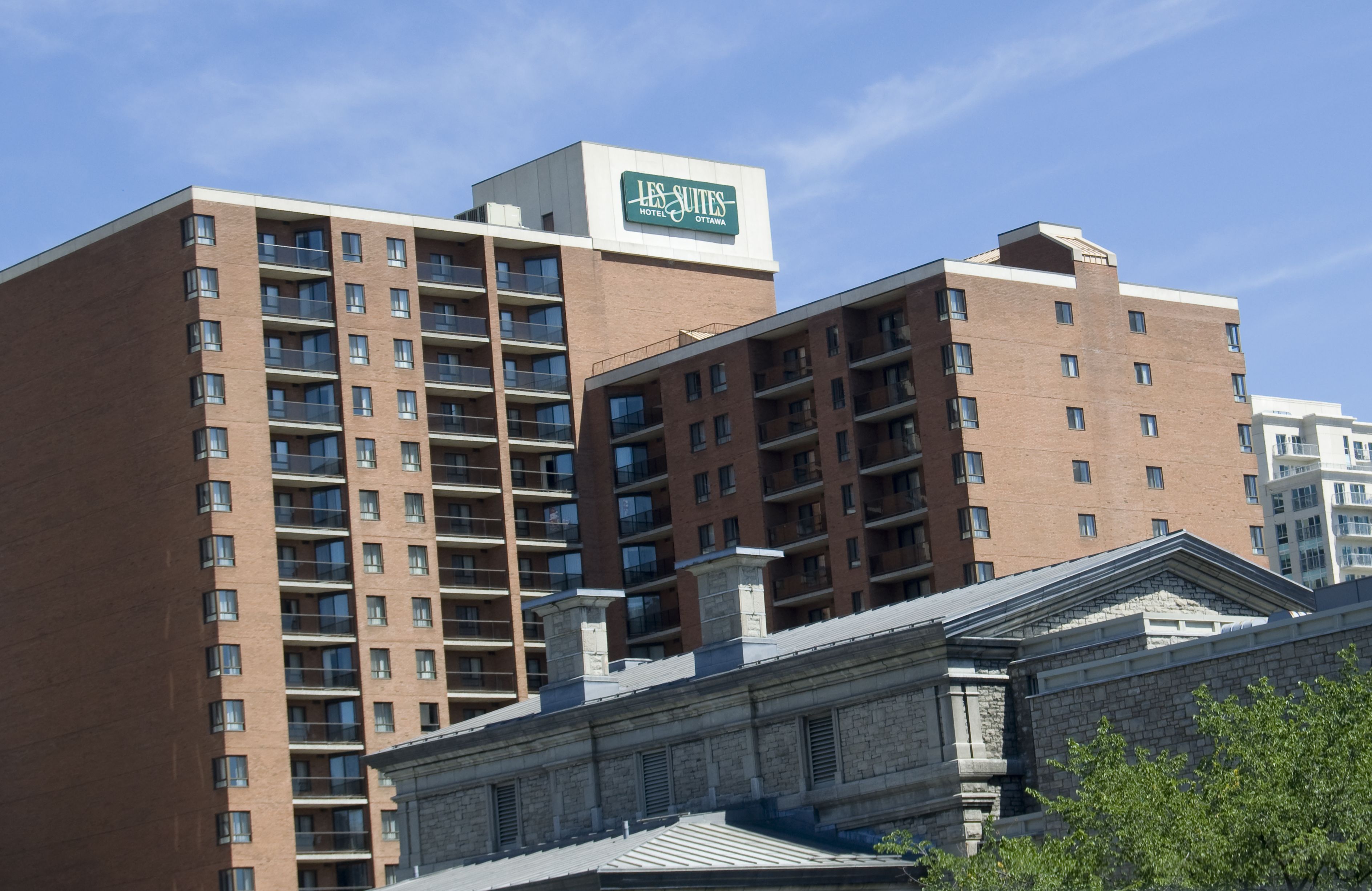Un hotel de varios pisos con un letrero llamativo que dice "Les Suites Hotel Ottawa". El edificio presenta un estilo arquitectónico moderno con una combinación de fachadas de ladrillo y piedra.