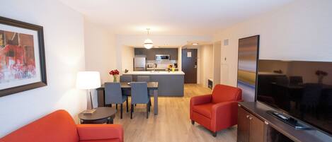 A modern living room with a sofa, a TV, and a dining area with chairs and a table.