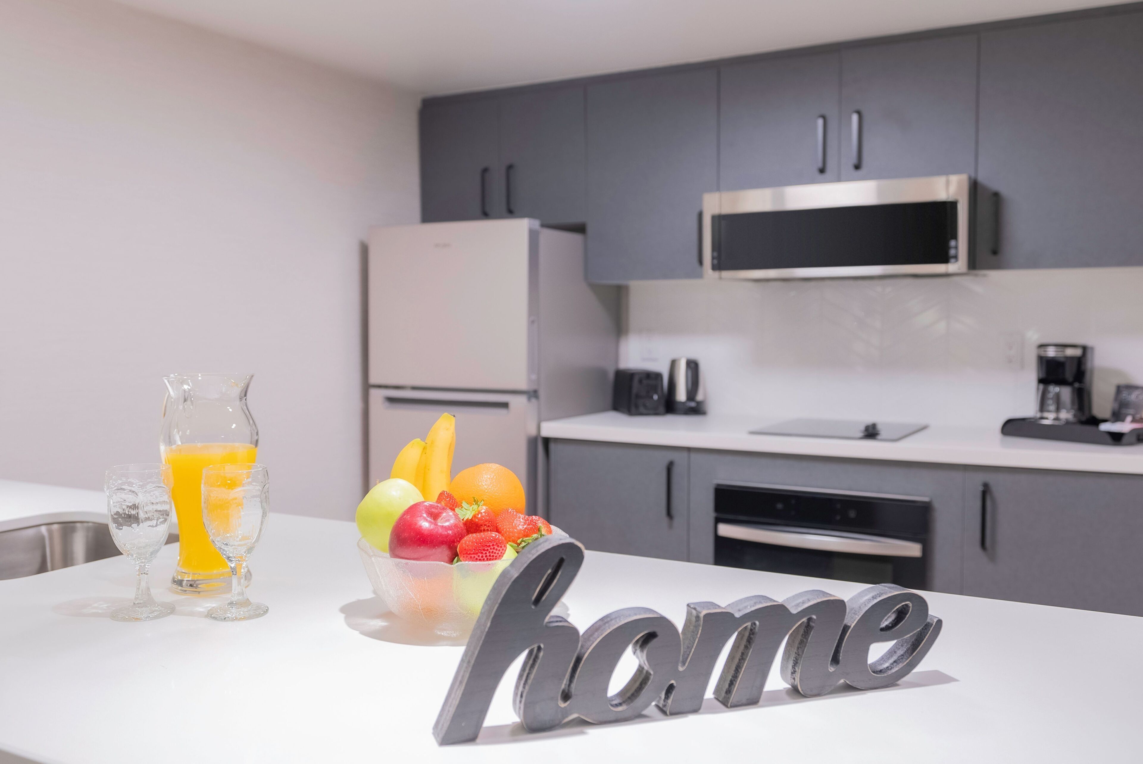 A modern kitchen with grey cabinets, a stainless steel microwave, and a white countertop.
