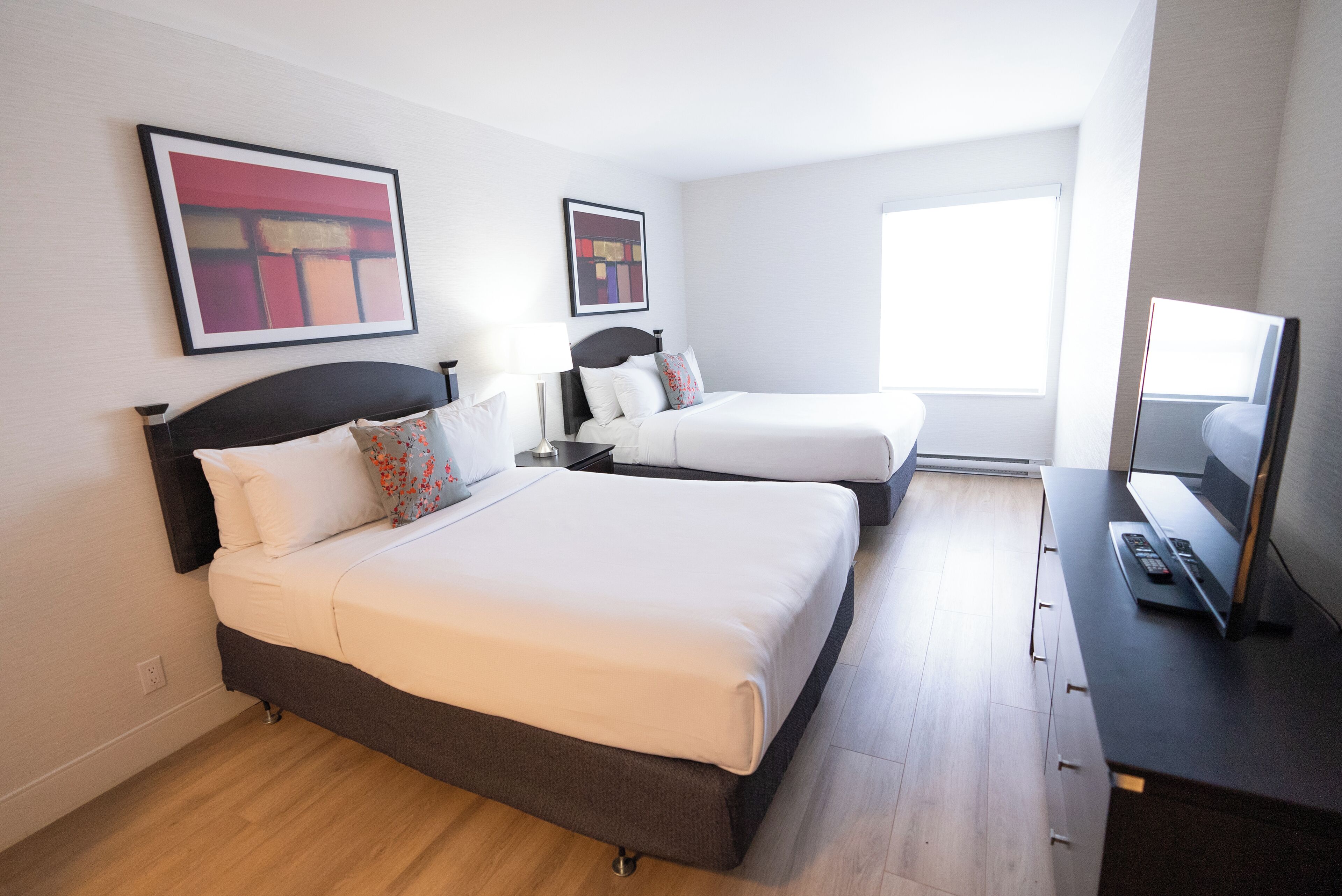 Ein Hotelzimmer mit zwei Betten, einem Fernseher und Bildern an den Wänden.