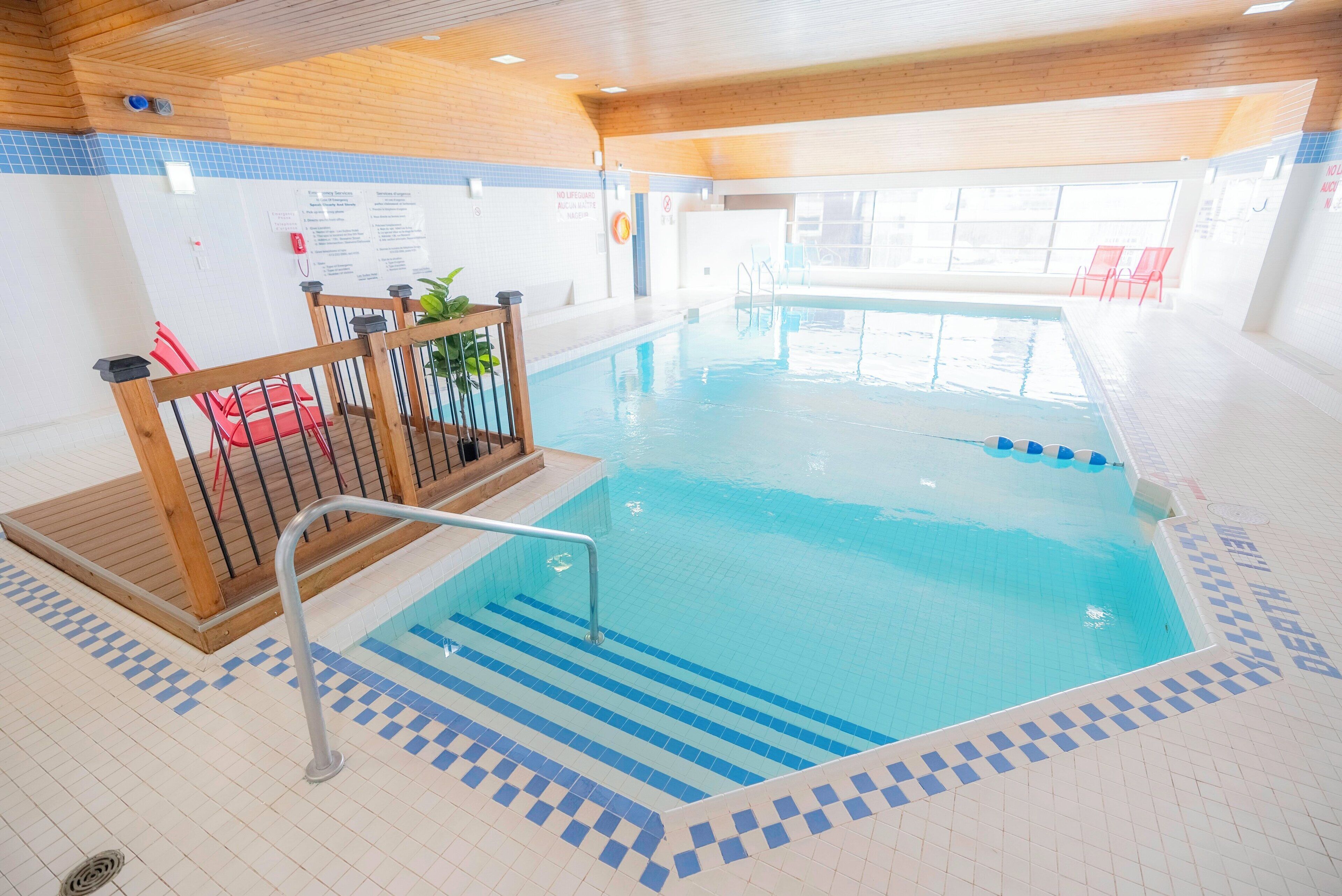 An indoor swimming pool with clear blue water, wooden deck, and tiled steps leading into the pool.