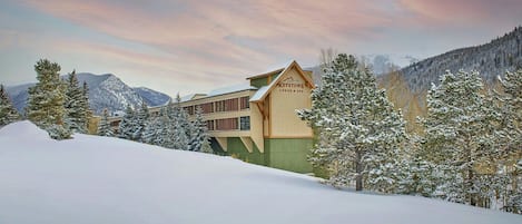 A lodge with a sign reading "Keystone Lodge & Spa" amidst snow-covered trees and mountains.