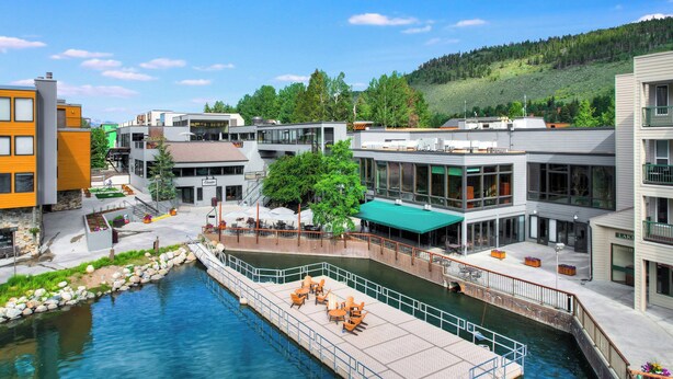 A riverside hotel with outdoor seating, a dock, and modern buildings.