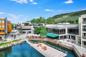 Un hotel a la orilla del río con terraza al aire libre, un muelle y edificios modernos.