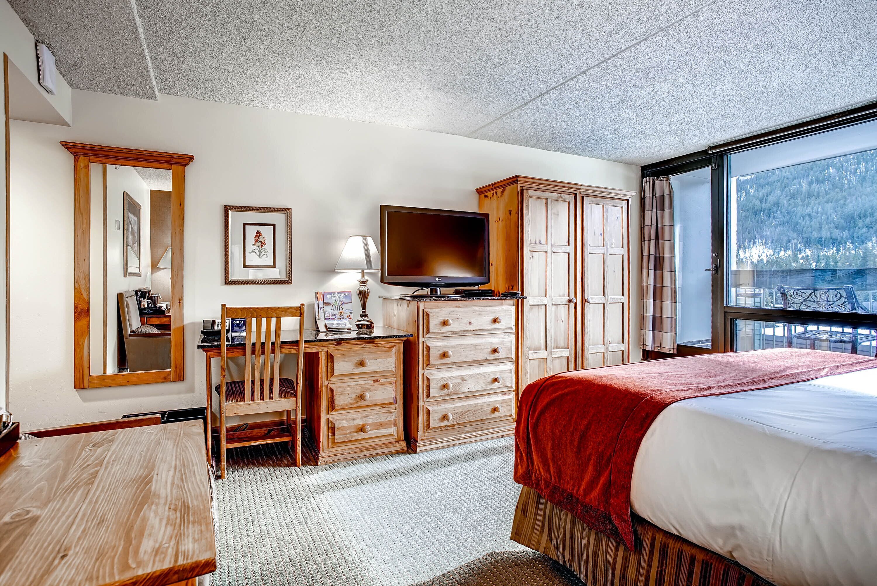 A hotel room with a bed, a desk with a chair, a television, and a wardrobe.