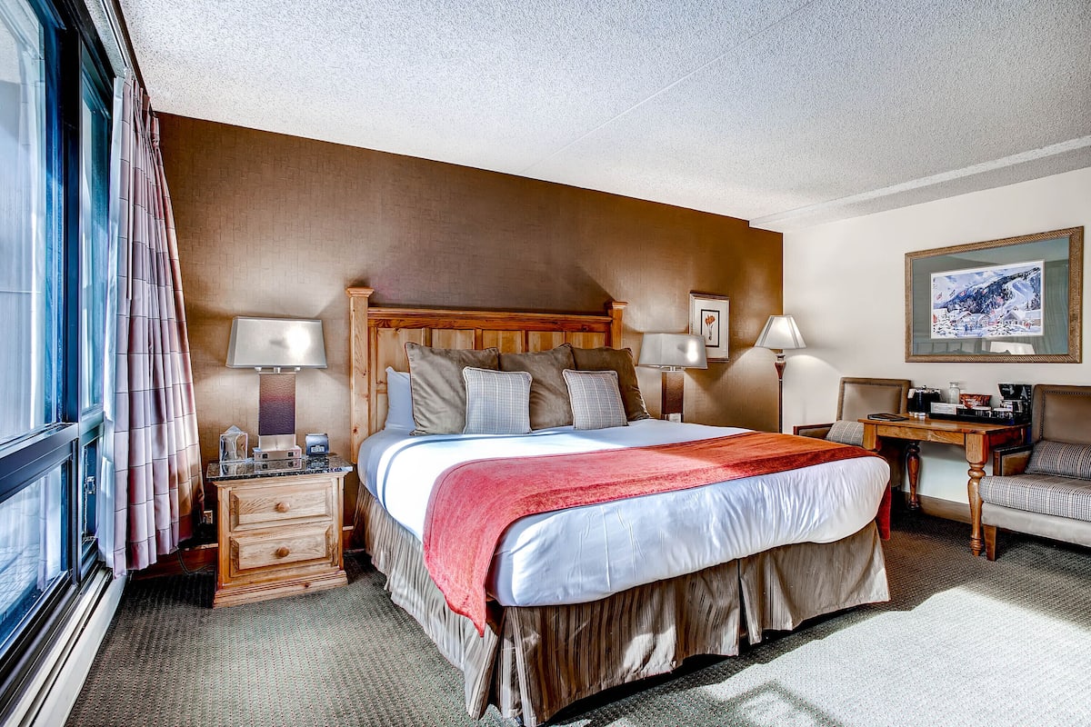 A hotel room with a large bed, bedside tables, a desk, and a chair.