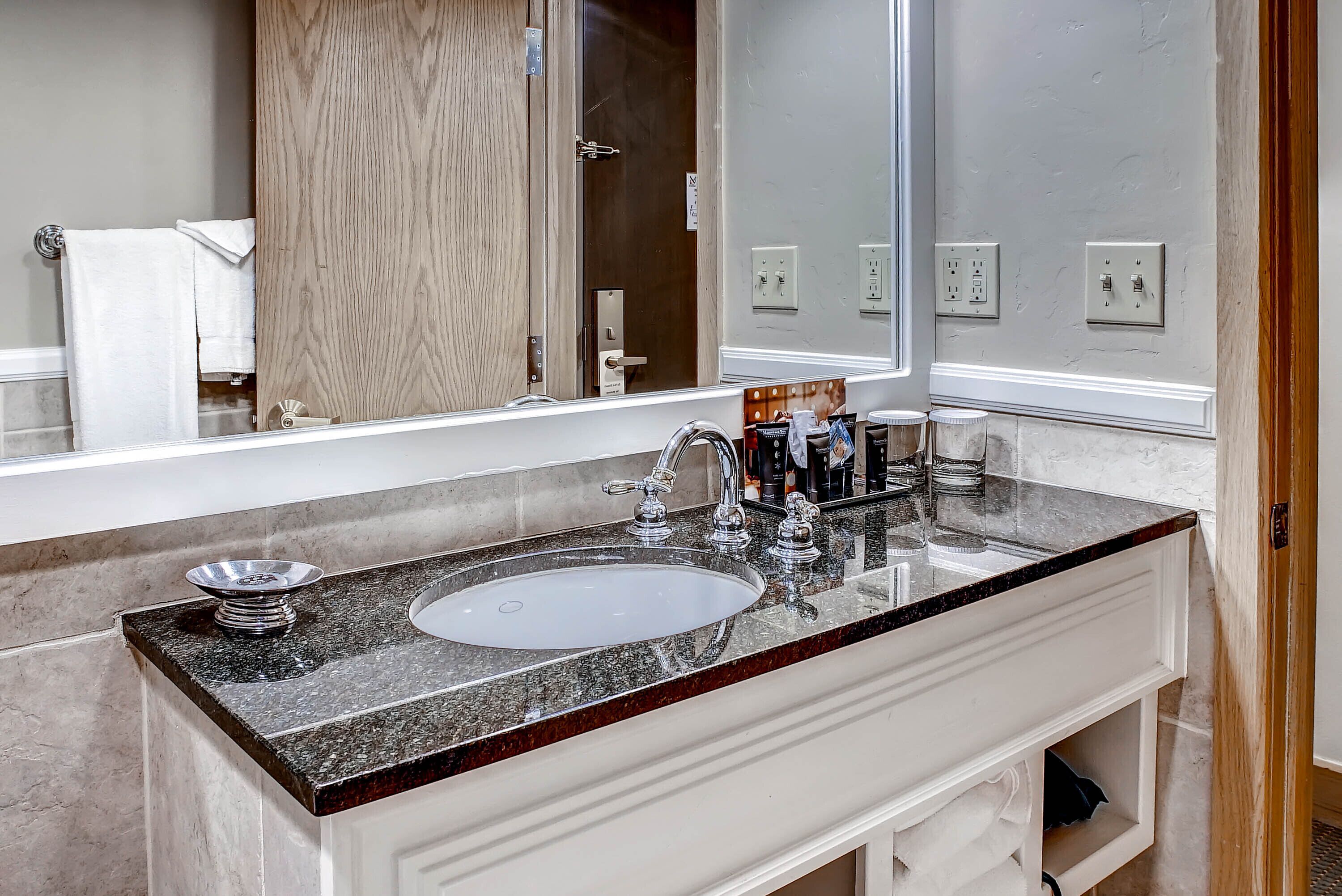 Une salle de bain avec un comptoir en granit, un lavabo blanc et un grand miroir.
