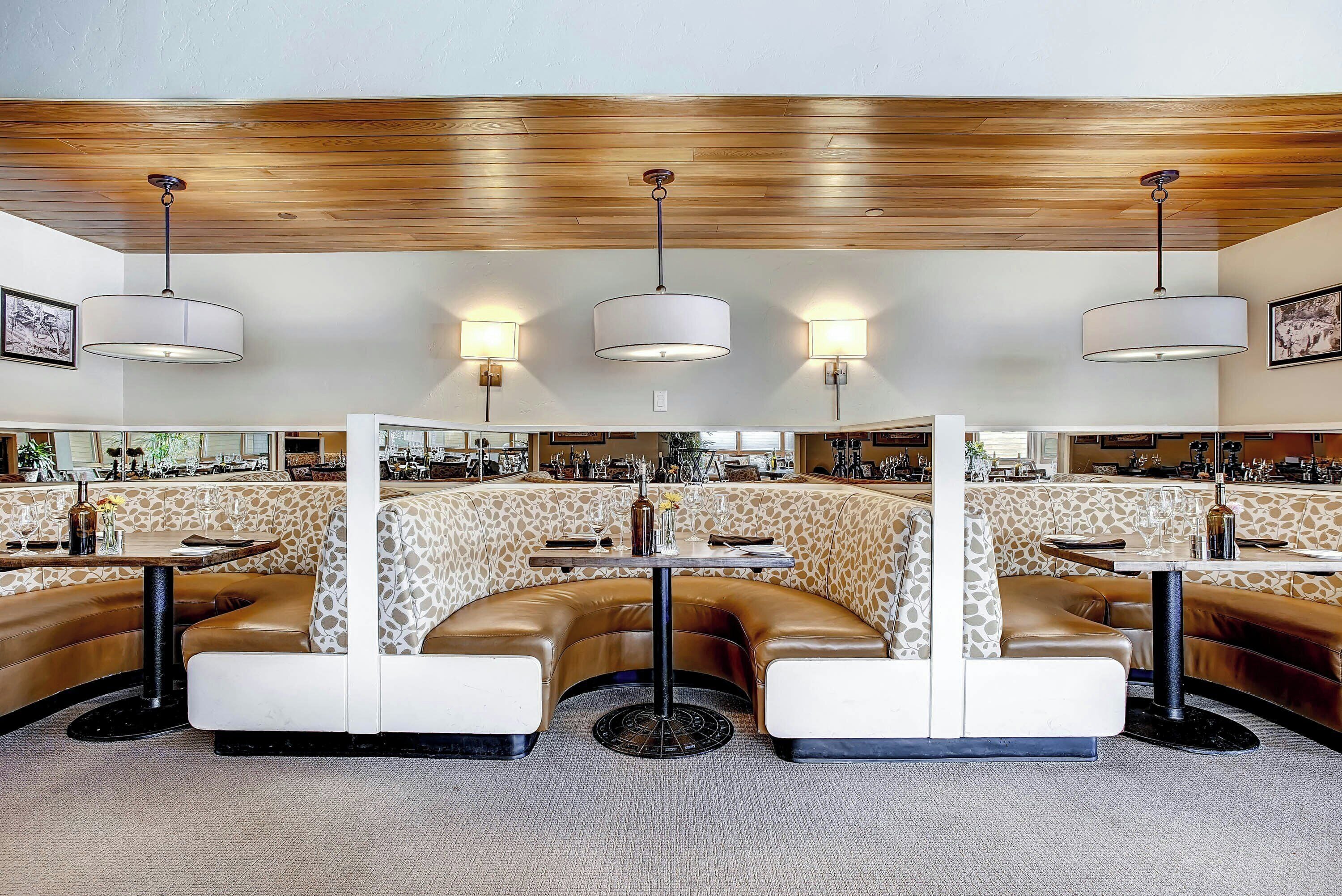 A restaurant with booth seating, pendant lighting, and a bar area in the background.