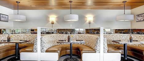A restaurant with booth seating, pendant lighting, and a bar area in the background.