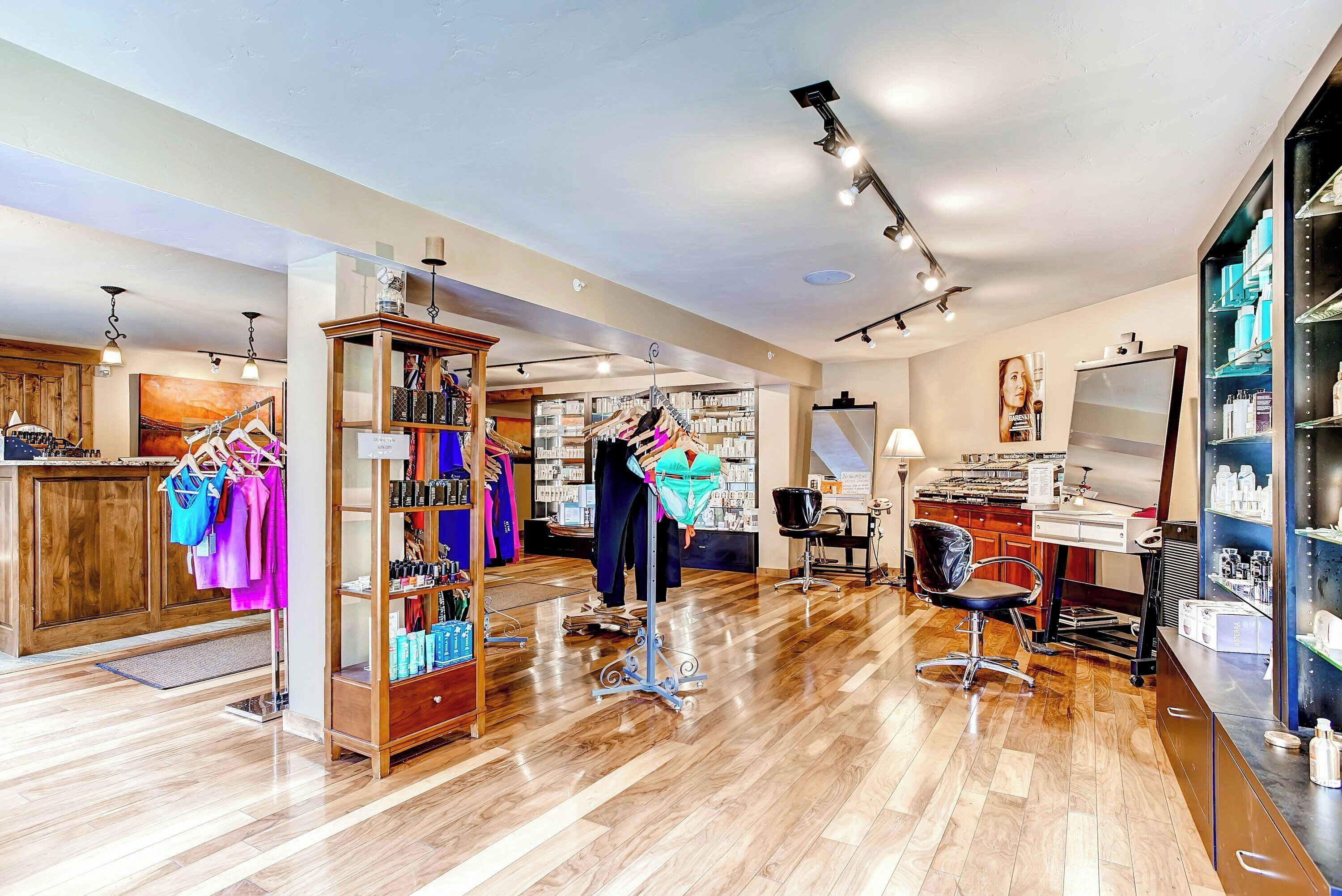 Un salon doté de planchers en bois, d’un espace dédié au lavage des cheveux et d’étagères remplies de produits capillaires.