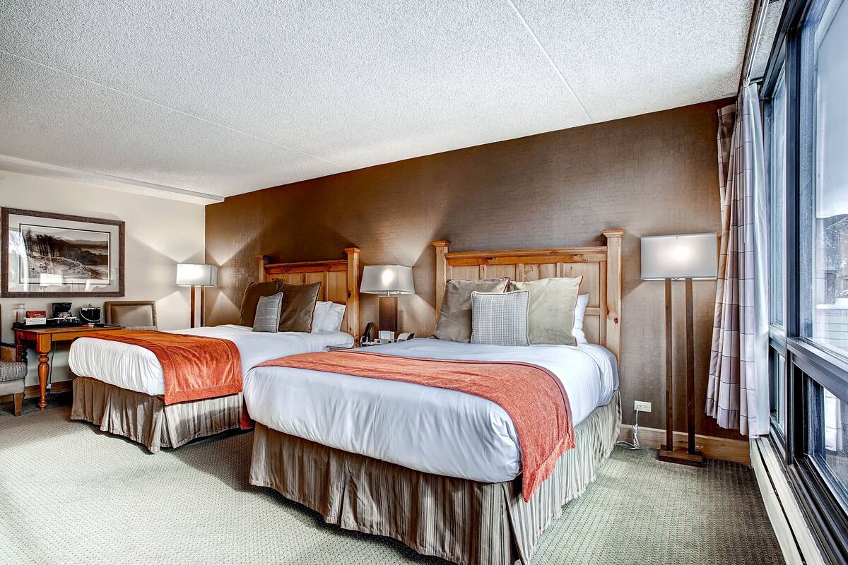 A hotel room with two beds, a desk, and a chair.