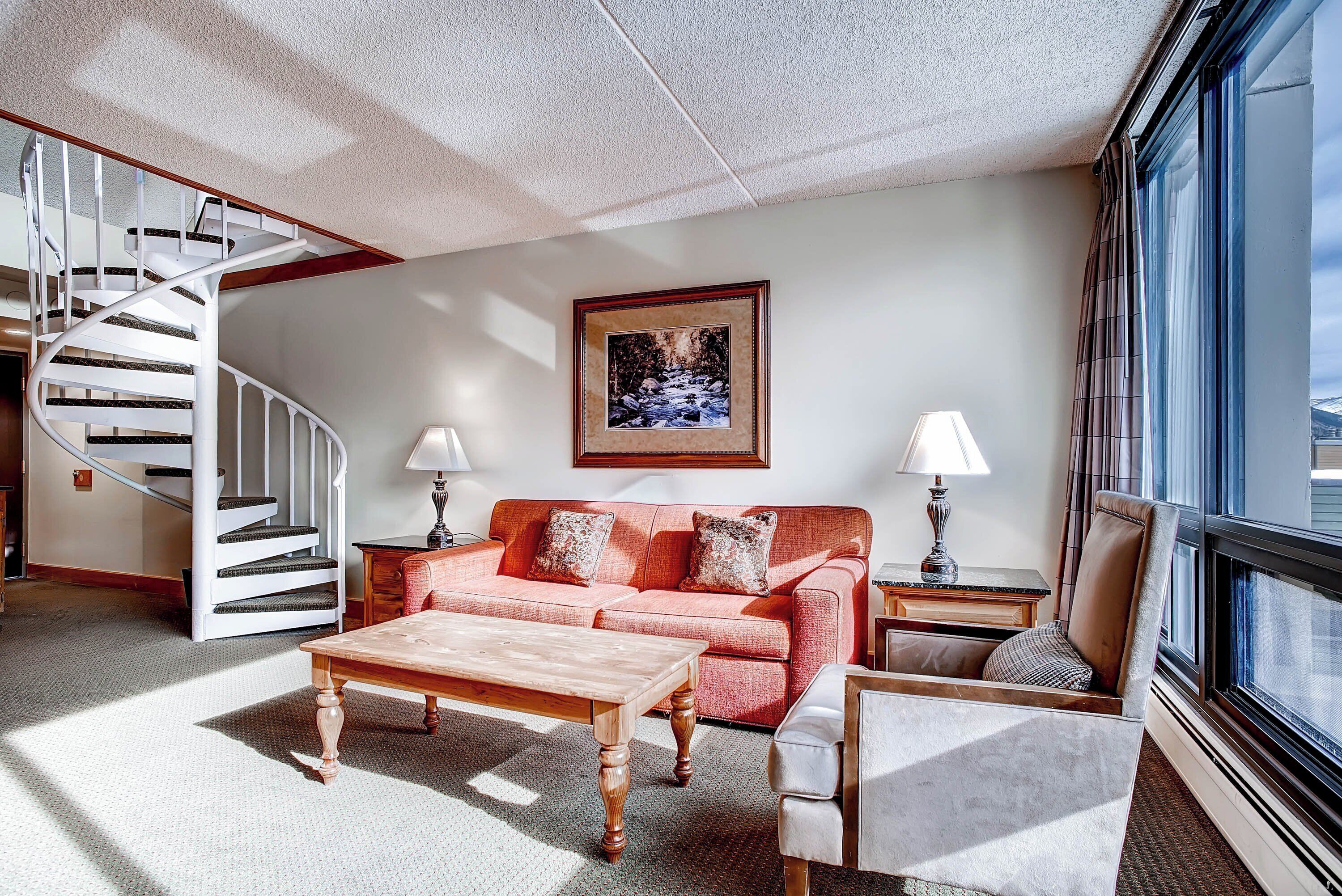 A living room with a staircase, a sofa, a coffee table, two lamps, and a framed picture on the wall.