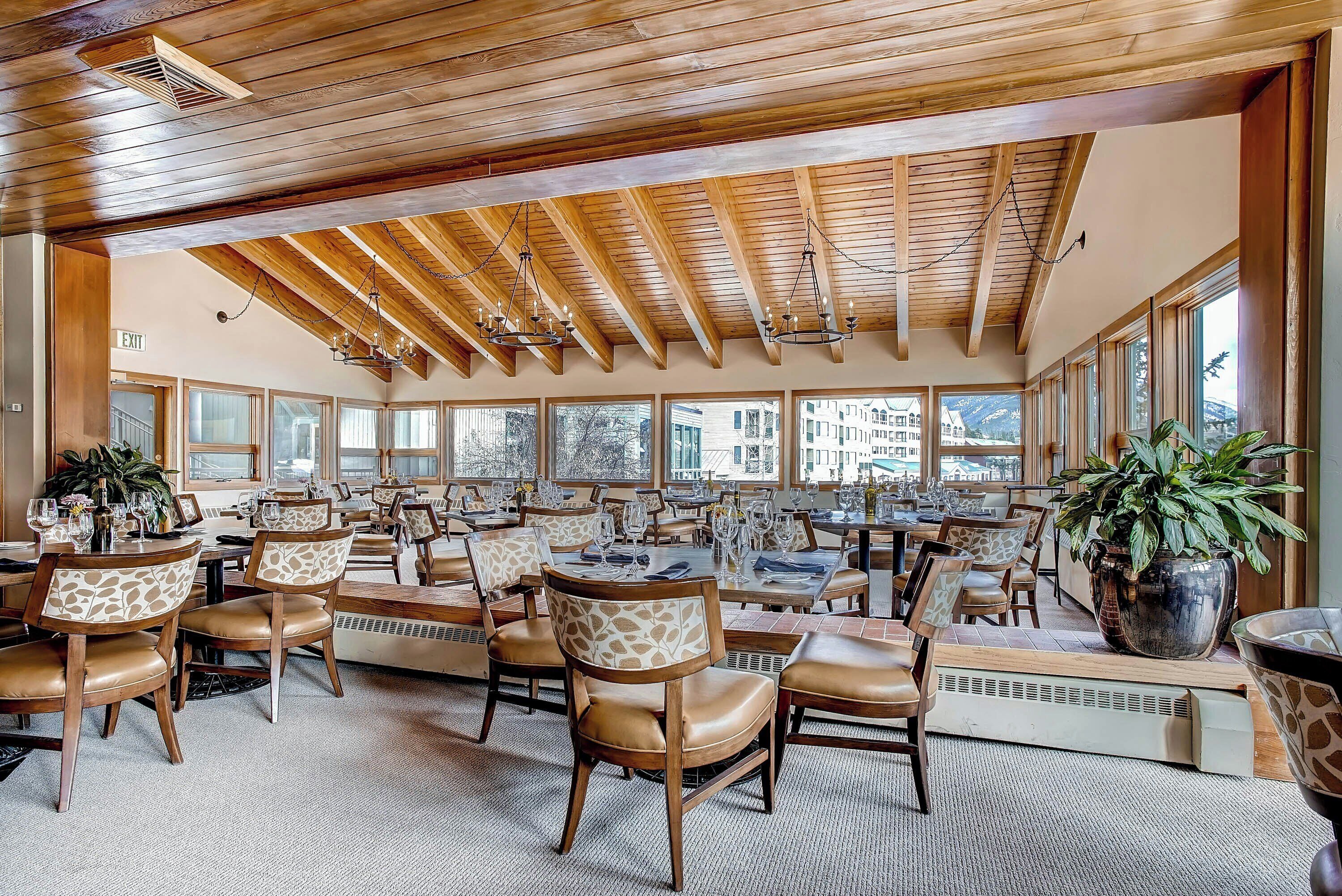 A spacious dining area with wooden beams, large windows, and leather chairs.
