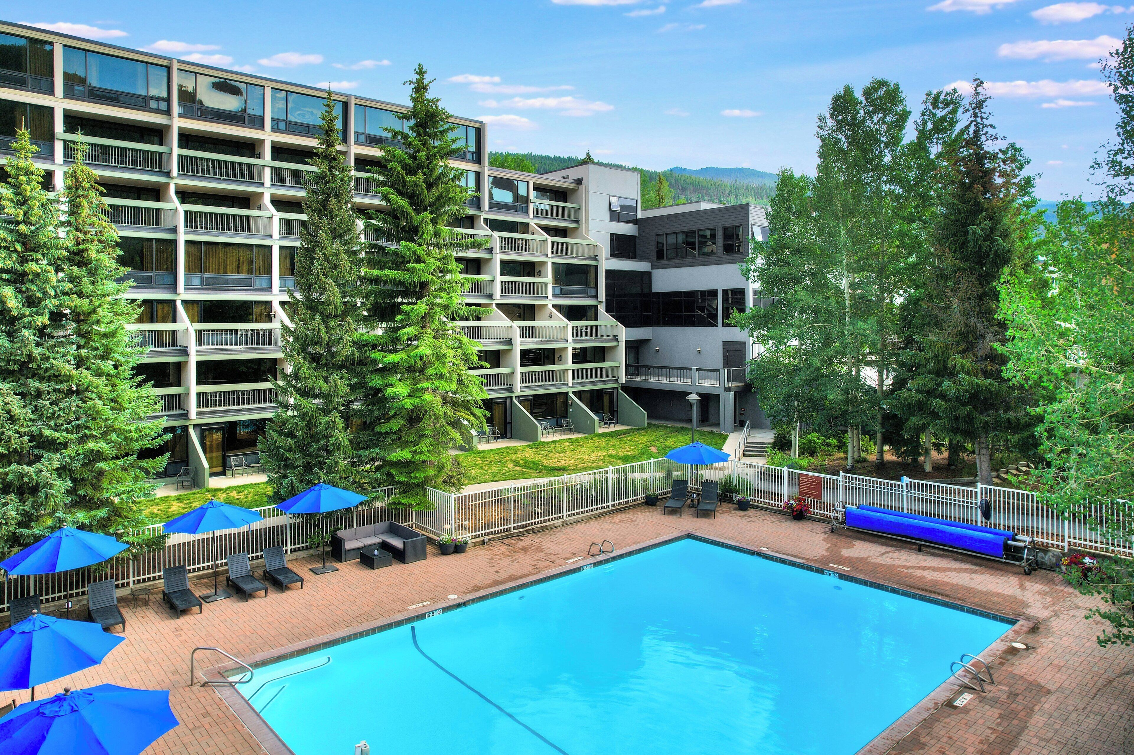 Un hotel moderno con piscina, zona de estar al aire libre y vistas del bosque circundante.