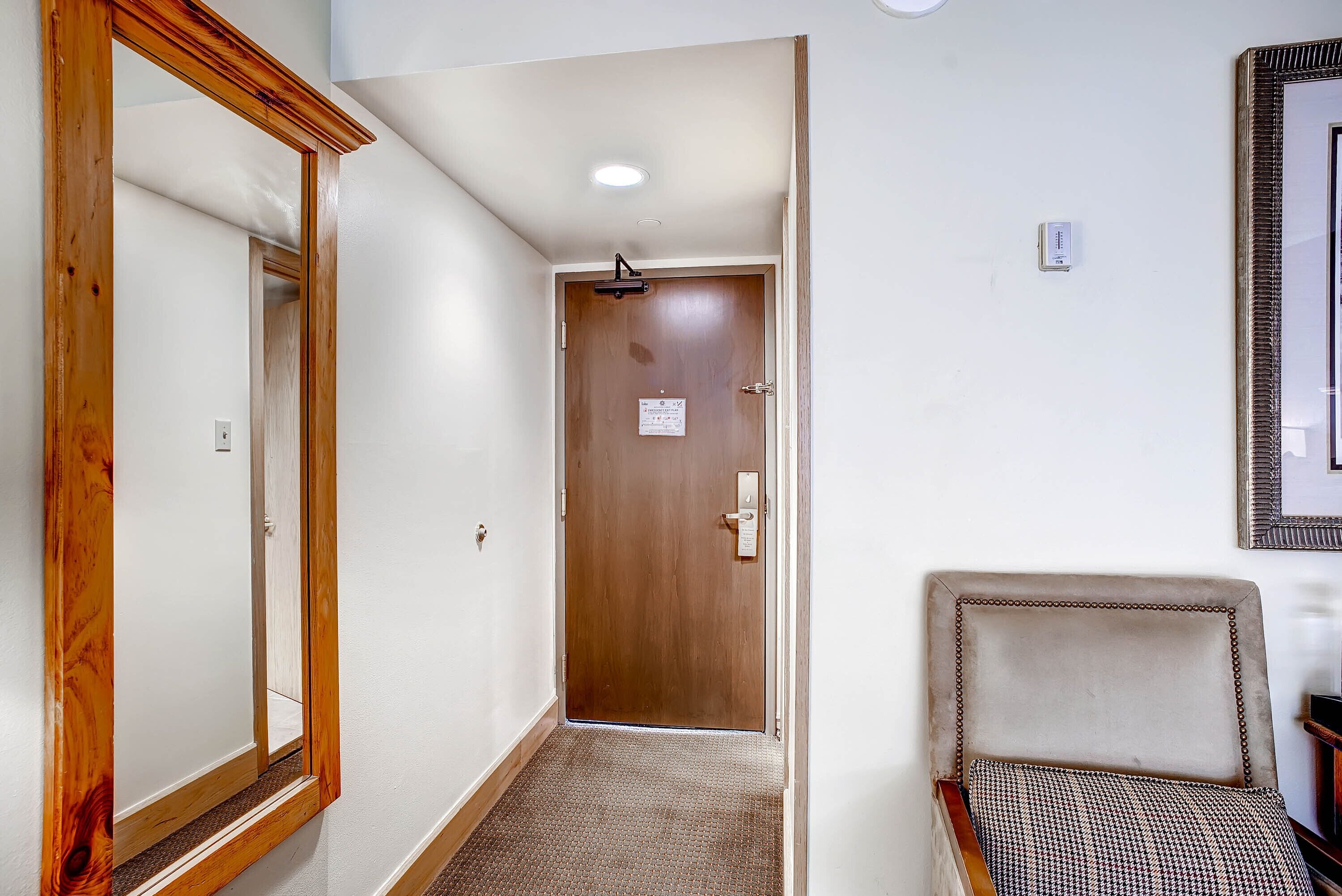 A hallway with a wooden door, a mirror, and a patterned chair.