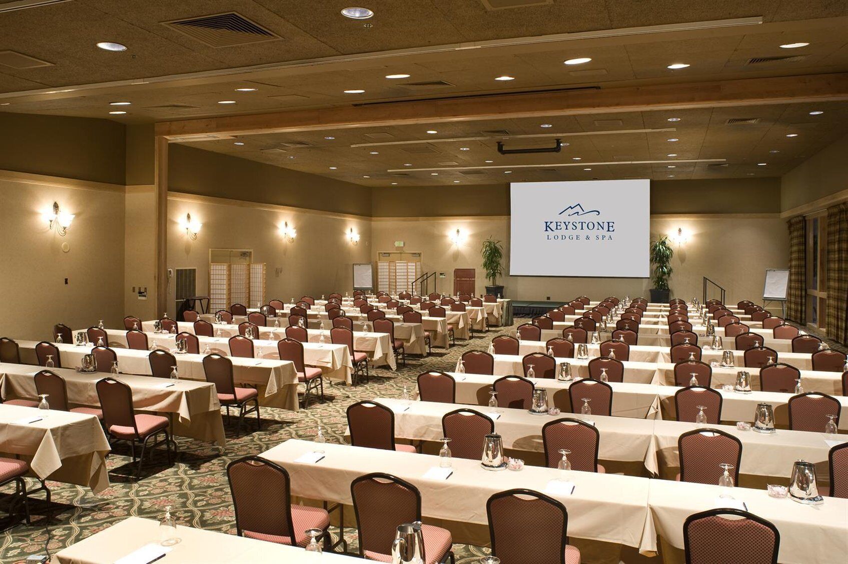 A large conference room with rows of tables and chairs, a screen displaying 'Keystone Lodge & Spa', and a carpeted floor.