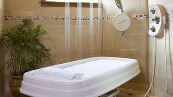 A bathroom with a white bathtub, a shower with a handheld showerhead, and a potted plant.