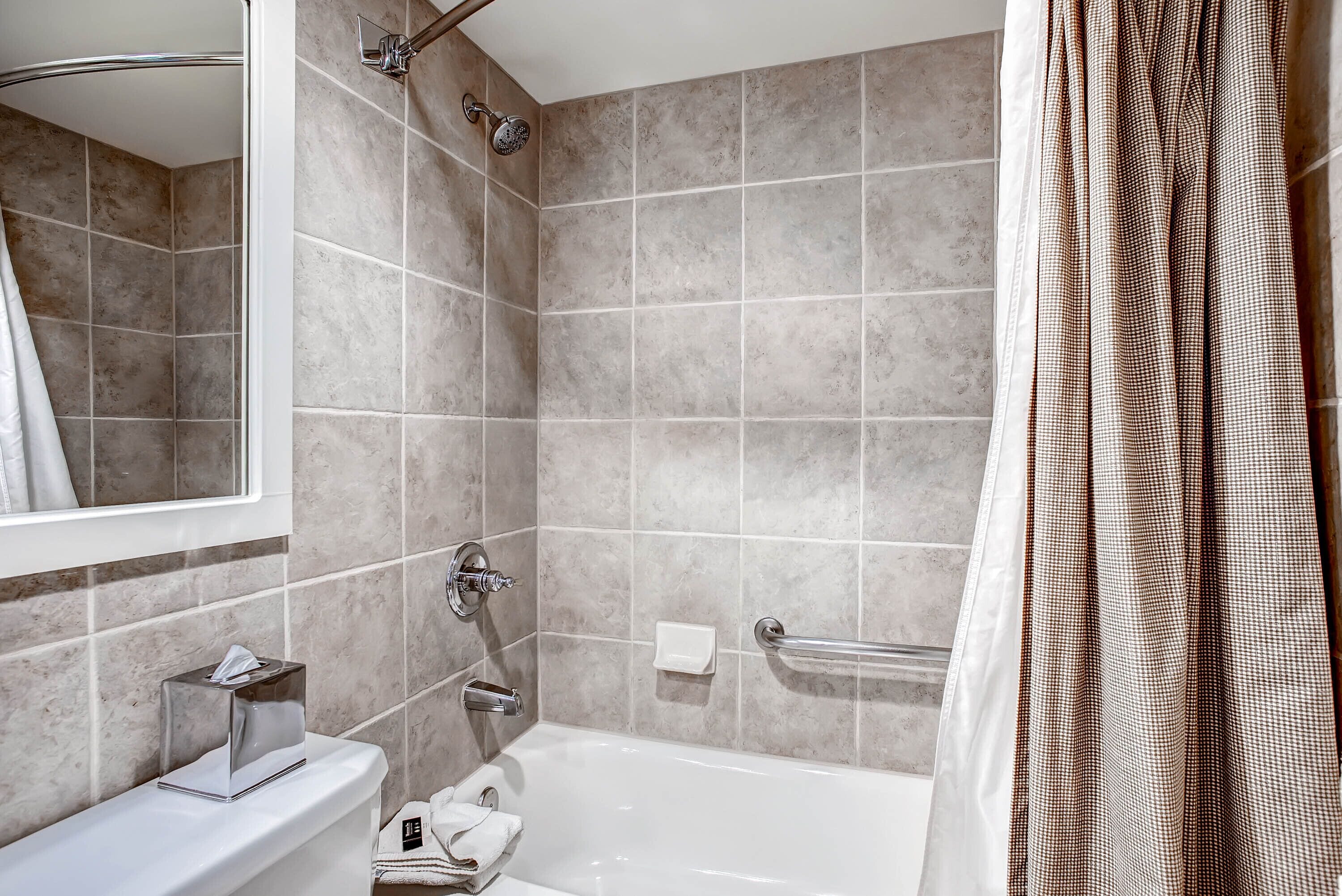 A modern bathroom with a bathtub, a vanity with a mirror, a towel rack, and a shower area.