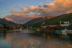 Un hotel frente al lago con una fuente, edificios y montañas al fondo.