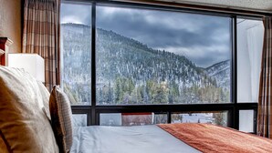A hotel room with a large window offering a view of a forested mountain.