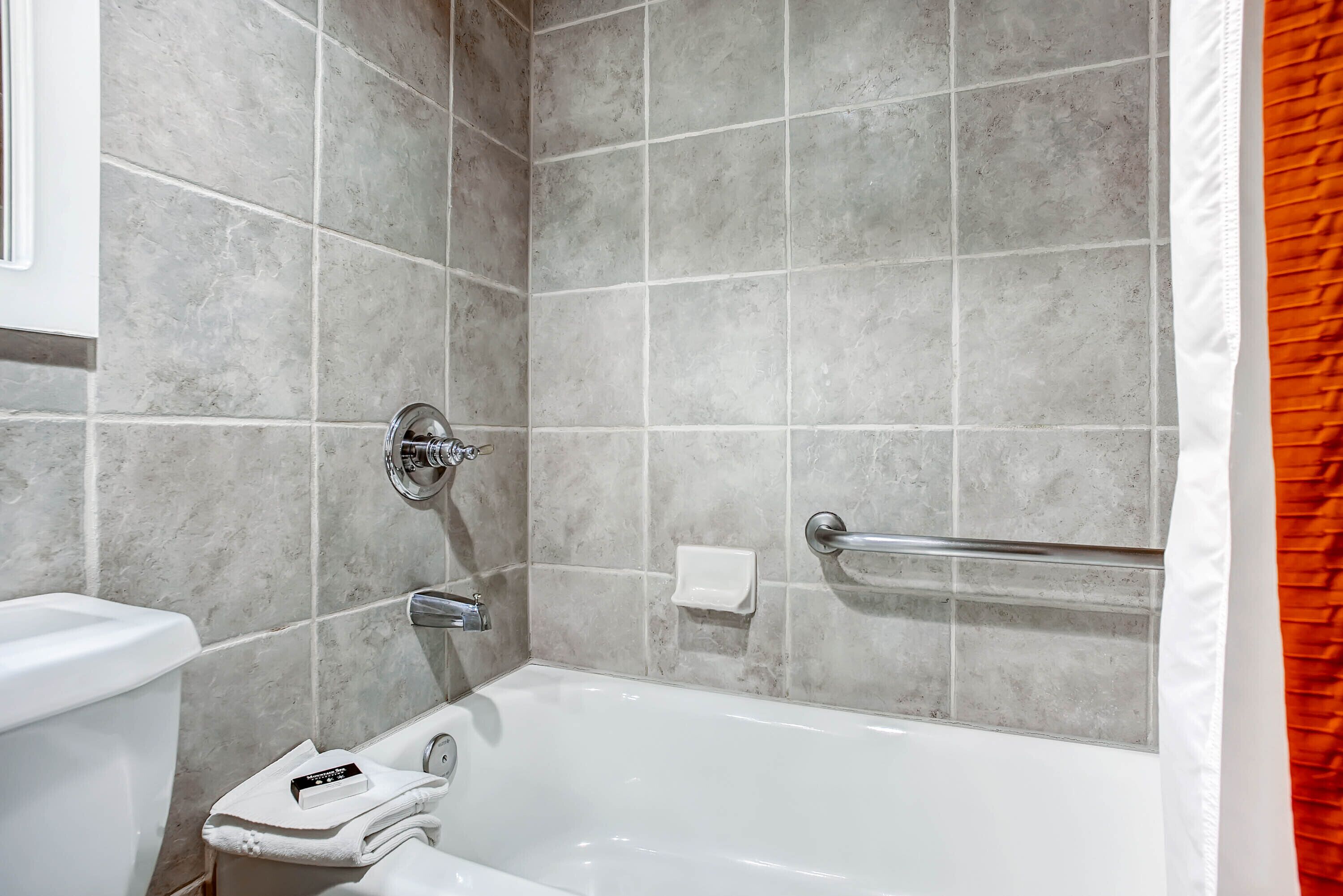 A bathroom with a bathtub, a toilet, and a handrail.