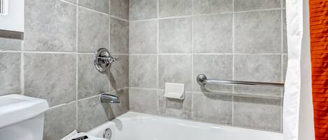 Een badkamer met een bad, toilet en een handgreep.