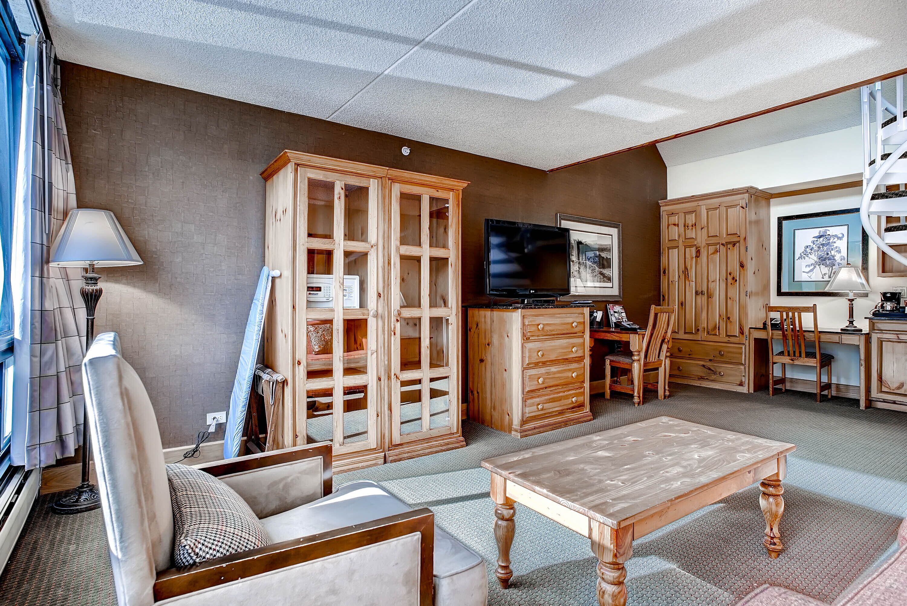 A living room with a wooden cabinet, a television, and a dining area with chairs and a table.