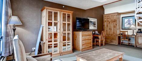A living room with a wooden cabinet, a television, and a dining area with chairs and a table.