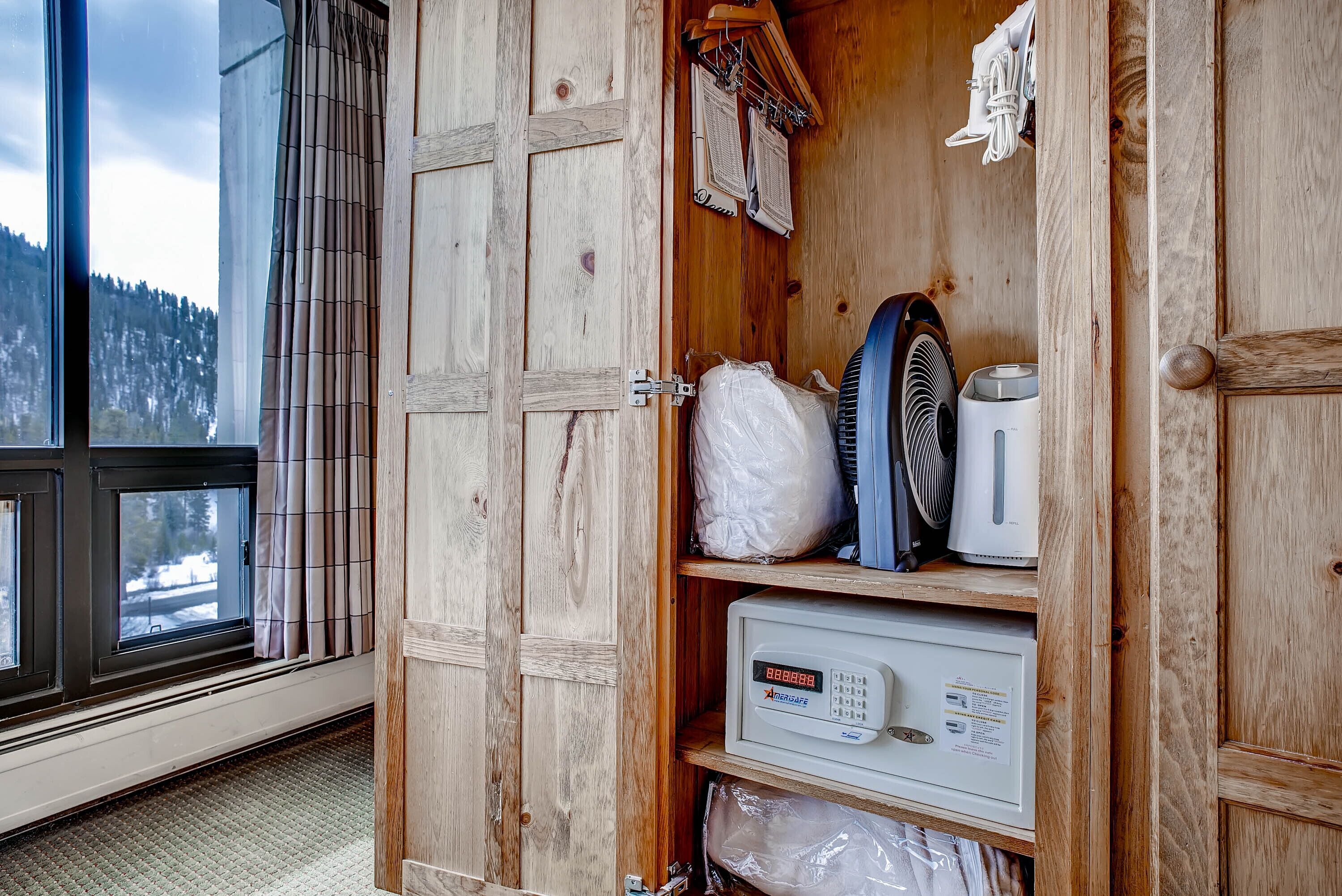 A wooden cabinet with a microwave, a fan, and some plastic bags.