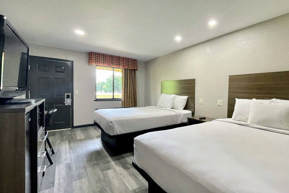 A hotel room with two beds, a desk, and a window with curtains.