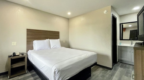 A hotel room with a neatly made bed, a bedside table with a phone, a small cabinet, and a mirror above the sink. - Best Value Inn (Bloomington)