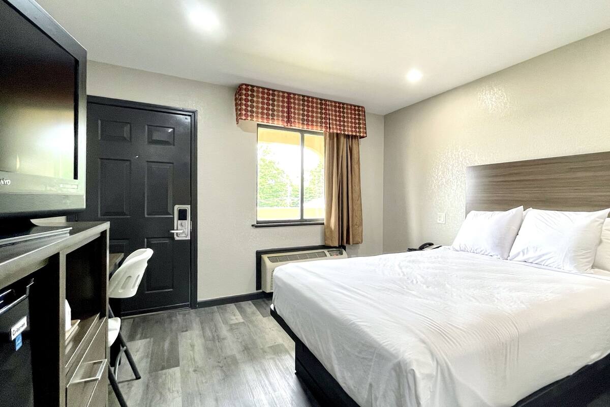 A hotel room with a bed, a desk, a chair, a television, and a window with curtains.