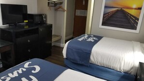 A hotel room with two beds, a desk with a TV, a microwave, and a painting of a sunset on the wall.