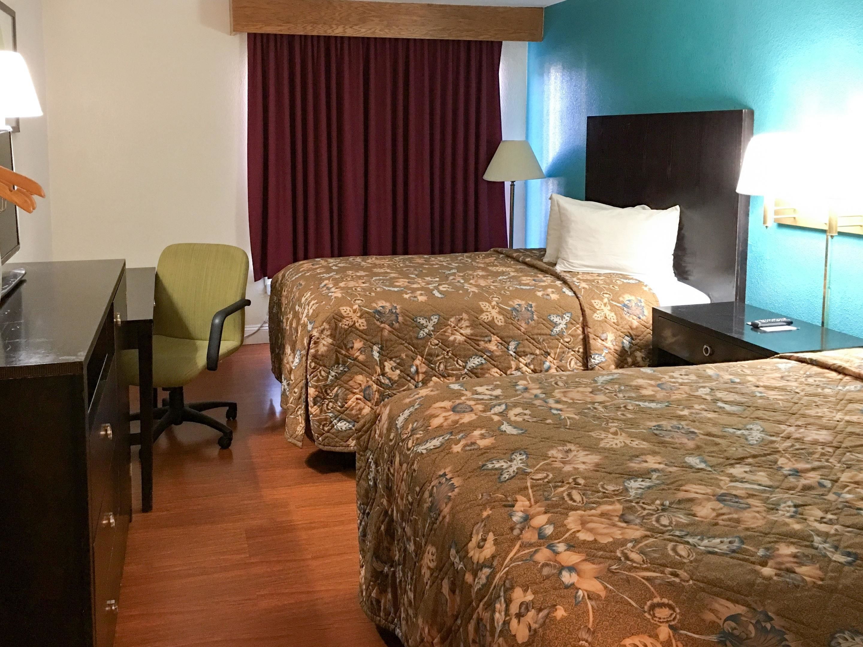 Une chambre d’hôtel avec deux lits, un bureau, une chaise, une lampe et un téléviseur.