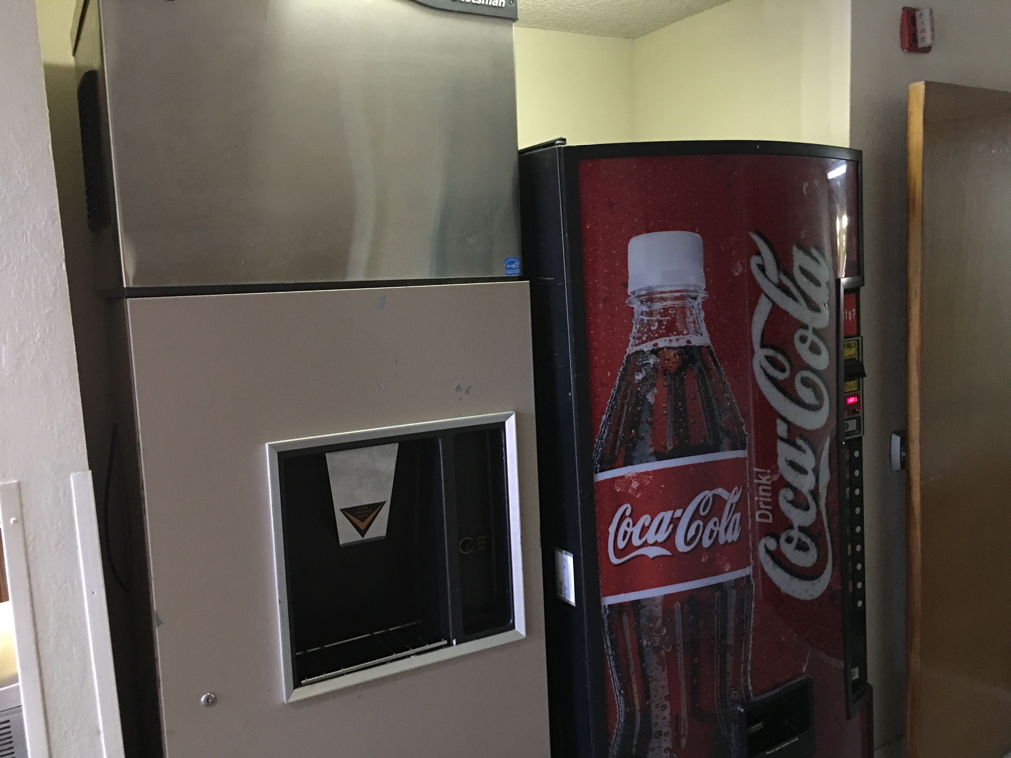 Una máquina expendedora con el logotipo de Coca-Cola y un refrigerador plateado.