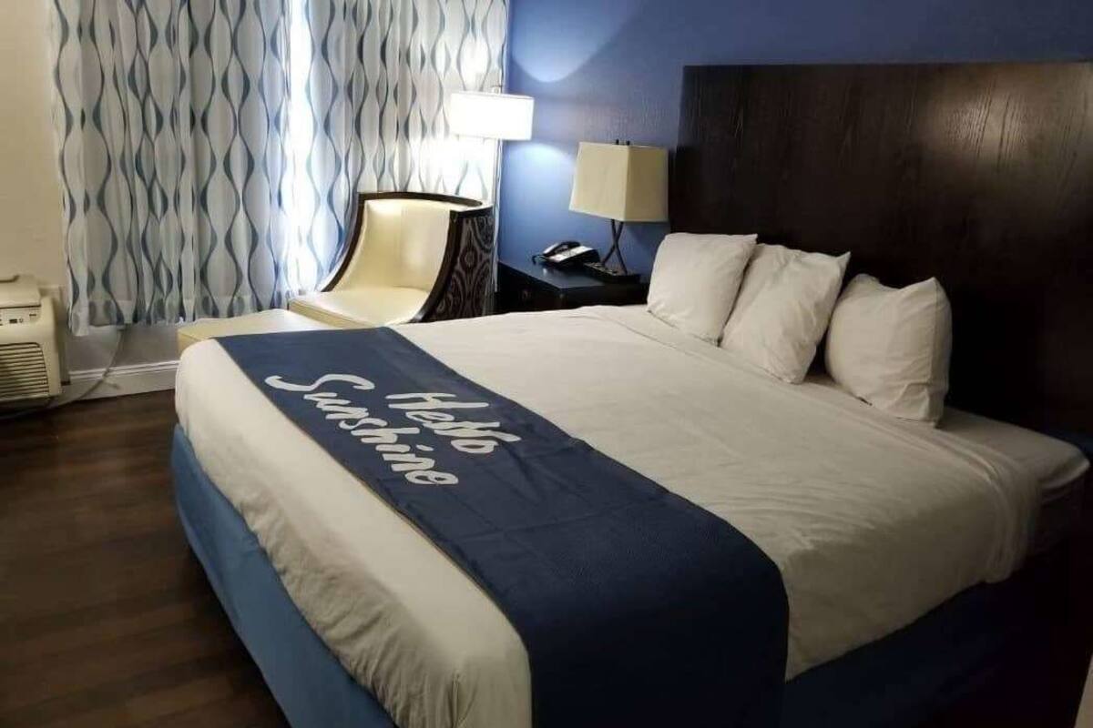 A hotel room with a bed, a chair, a lamp, and a wall with a patterned curtain.