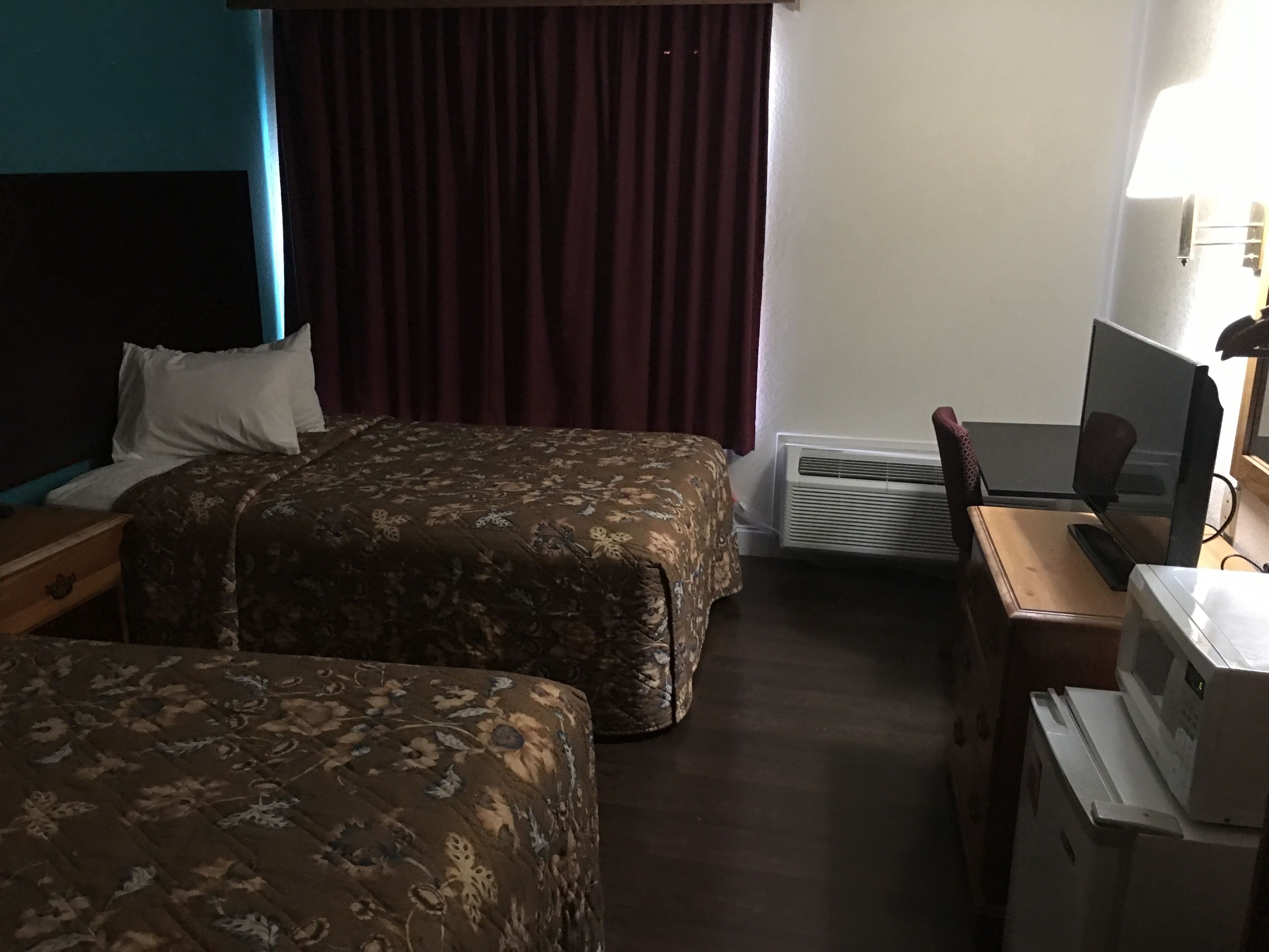 Une chambre d’hôtel avec deux lits, un bureau avec un ordinateur, une chaise et une fenêtre avec des rideaux.