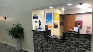 A reception desk with a check-in/out sign, a potted plant, a calendar, and a framed picture of a sunset.