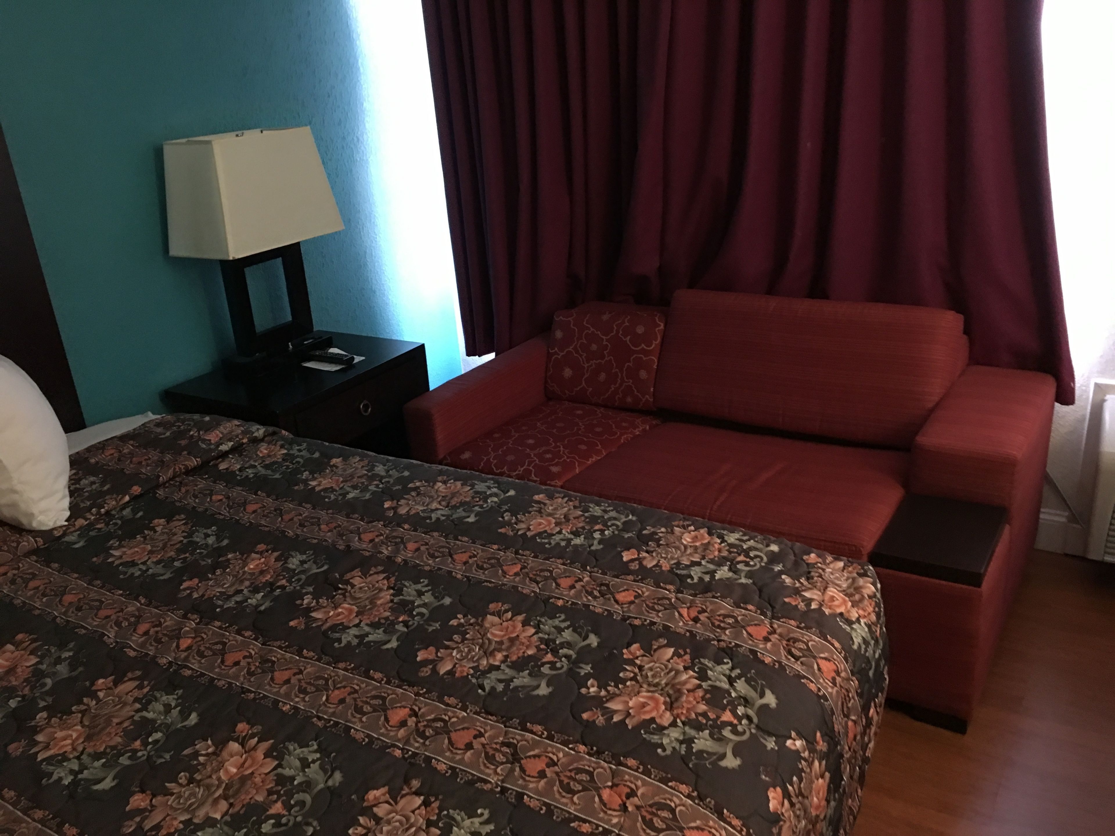 Un dormitorio con una cama, una mesita de noche, un sofá rojo y una ventana con cortinas.