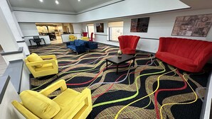 A spacious lobby with a patterned carpet, yellow and red chairs, and a modern kitchen in the background. - SureStay Plus by Best Western Mobile I-65 (Mobile)