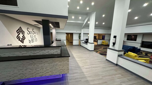 A modern hotel lobby with a reception desk, seating area, and a large wall with a logo. - SureStay Plus by Best Western Mobile I-65 (Mobile)