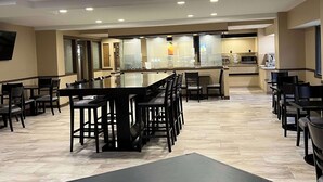A spacious dining area with multiple tables and chairs, a kitchen in the background, and a modern ceiling design. - SureStay Plus by Best Western Mobile I-65 (Mobile)