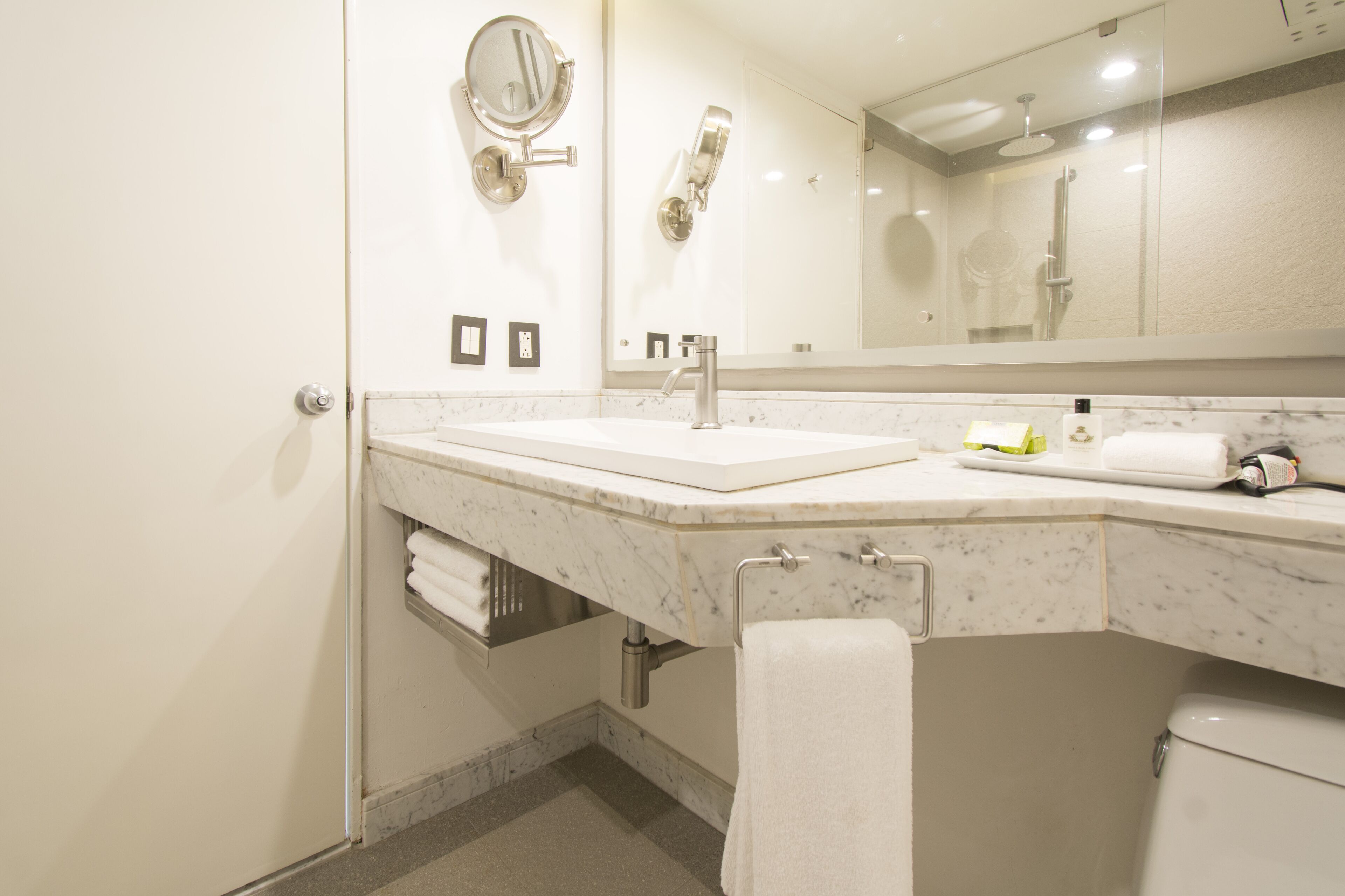 A modern bathroom with a marble sink, a large mirror, a towel rack, and a toilet.