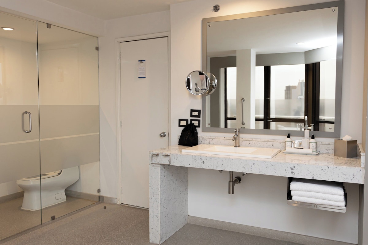 Un baño moderno con cabina de ducha de vidrio, inodoro blanco, lavabo de mármol y un espejo grande.