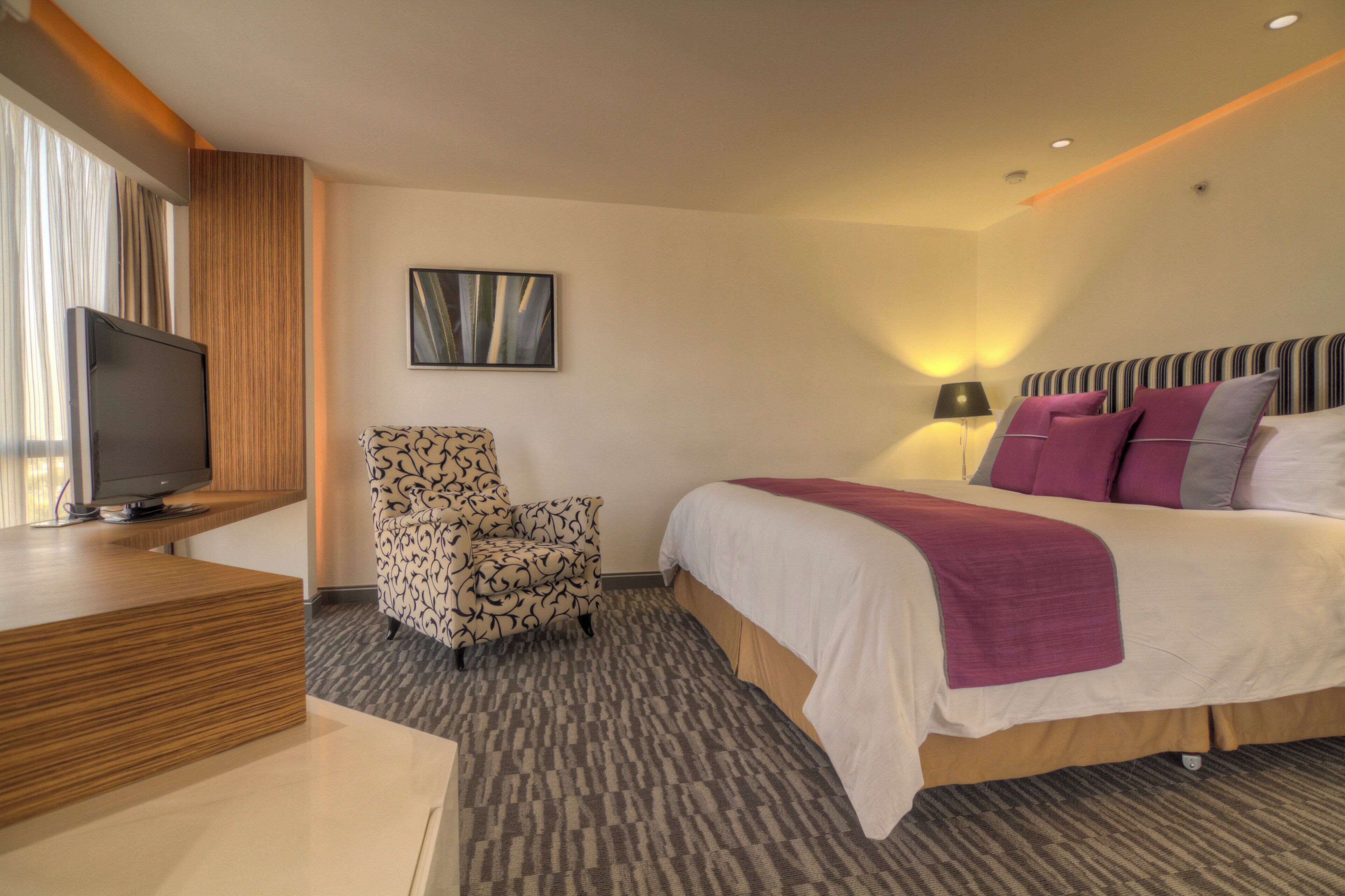A hotel room with a bed, a chair, a television, and a wall-mounted artwork.